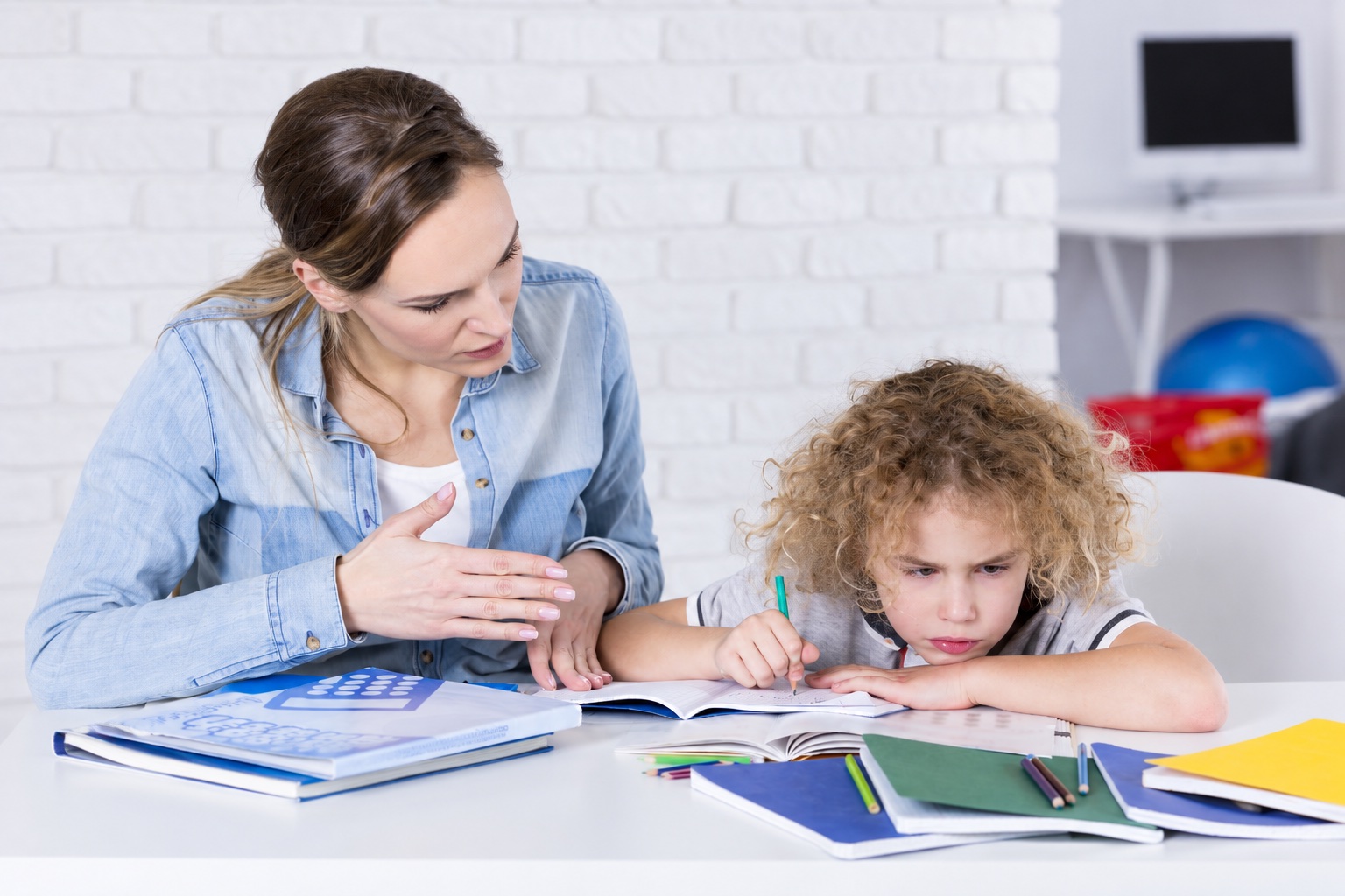 A mother and child working together at a table with an open notebook.